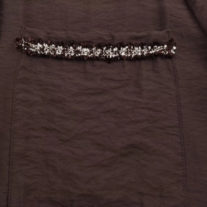 Dettaglio tasca di camicia marrone con finiture decorative di frange intrecciate