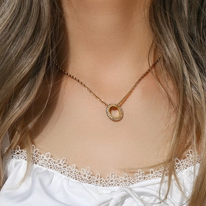 Detail shot of a gold twist chain necklace with a sparkling round zircon pendant on a model