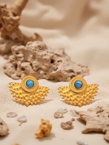 Macro detail of fan-shaped gold earrings with turquoise stone on a sandy background