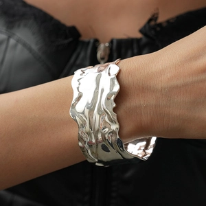 Detail of silver wavy metal cuff bracelet with liquid texture on model wearing black leather