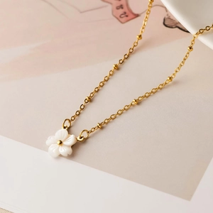 Detailed close-up of golden thin chain necklace with a white cherry blossom flower pendant