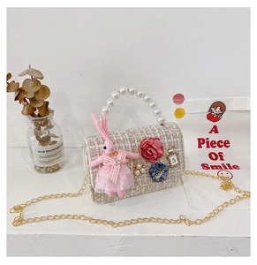 Detail of tweed crossbody bag with pink rabbit plush, pearls, and metal chain strap