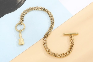 Detailaufnahme von goldenem Doppelkettenarmband mit Gitarrenanhänger und OT-Verschluss