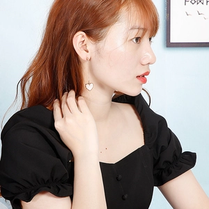Detail of long gold heart drop earrings with white enamel inlay on a female model