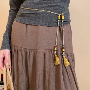 Detail of woven waist belt with tassels and beads over a dark grey sweater and skirt