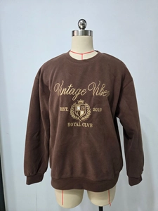 Detailaufnahme der goldenen Stickerei auf einem dunkelbraunen Rundhals-Sweatshirt