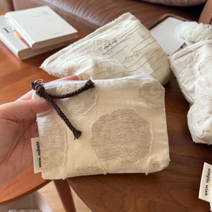 Detail of beige cotton linen pouch with 3D floral texture and zipper pull strap