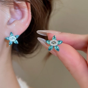 Macro detail of blue crystal flower earrings with S letter zircon center on ear