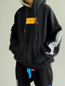 Detail of black oversize hoodie with yellow chest patch and striped sleeve cuffs