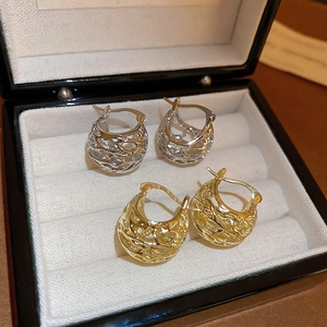 Close-up of gold and silver hollow woven texture basket hoop earrings on white velvet