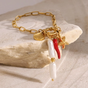 Dettaglio del bracciale dorato con perla, peperoncino rosso e ciondoli marini su pietra