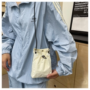 Detail of a minimalist cream-colored nylon crossbody bag with drawstring and black cord strap