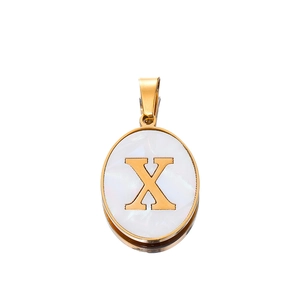 Macro shot of oval gold pendant with letter X inlay on white shell texture surface