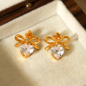 Macro shot of gold bow stud earrings with heart-shaped sparkling zircon on beige velvet