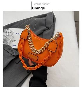 Detail of orange fashion underarm bag with gold chain strap and woven handle on grey blazer