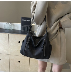 Detail of black faux leather tote bag showing soft pleated texture and side zippers