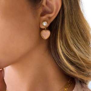 Close-up of pink heart pearl earrings worn by a model showing gold plated details