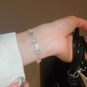 Close-up of elegant gold zircon bracelet on wrist with white satin and black clutch bag