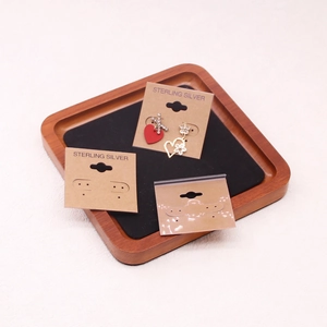 Close-up of heart stud earrings displayed on PVC cards within a wooden jewelry tray