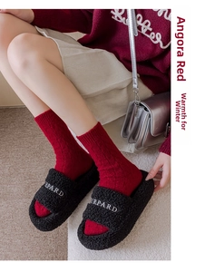 Close-up of black plush slippers with white embroidery worn with red festive winter socks