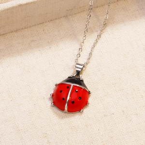 Close-up of a red ladybug pendant with black enamel dots on a fine silver chain