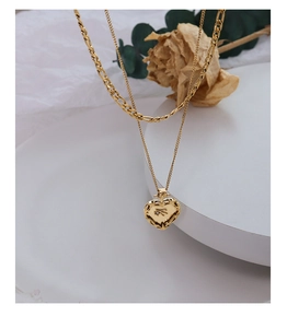 Détail d'un collier doré double rang avec pendentif cœur en relief au style vintage