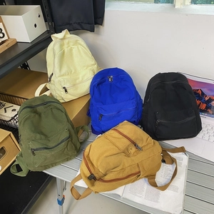 Mini zaini in tela in cinque colori tra cui beige, blu e verde su una scrivania