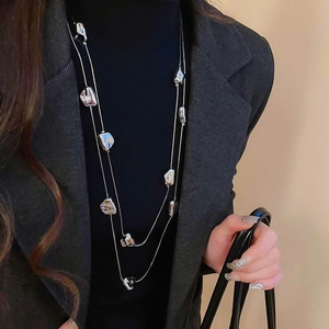 Dettaglio della collana argentata a doppio strato con ciondoli su maglione nero a collo alto