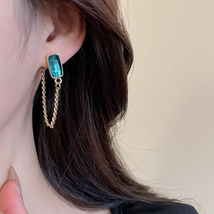 Detailed view of elegant gold drop earrings featuring a rectangular emerald green gemstone