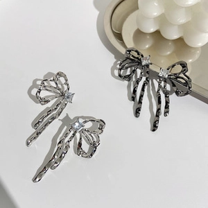 Close-up of liquid metal bow earrings with dangling tassels and square zircon center