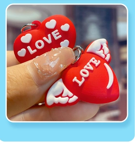 Detailed macro view of two red heart PVC keychains with LOVE lettering and wings relief