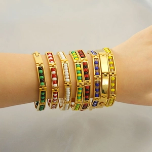 Detail view of gold beaded bracelet set with vibrant colorful charms on a person's wrist