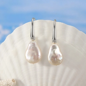 Baroque irregular pearl drop earrings displayed on a white scallop shell with ocean theme