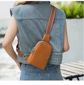 Close-up of brown leather chest bag with double zippers and striped nylon shoulder strap