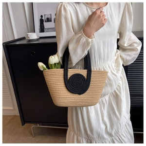 Detail of beige hand-woven tote bag with black spiral patterns held by a model