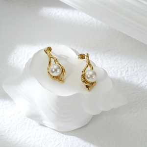 Detail von 18 Karat Gold-Ohrringen mit runder Perle auf Muschel-Requisiten-Hintergrund