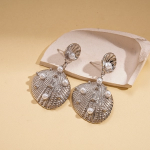 Detail of silver shell earrings with faux pearls on a textured background