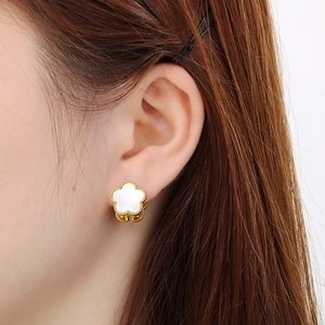 Close-up of golden clover earrings with white mother-of-pearl and beaded edges on ear