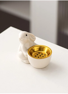 Close-up of a white ceramic rabbit incense burner holding a gold metal aromatherapy bowl