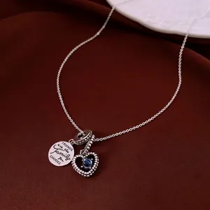 Collana minimalista in argento con gemma a cuore e ciondolo inciso su sfondo di seta