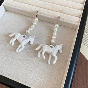 Détail de boucles d'oreilles cheval avec perles blanches dans un écrin en velours