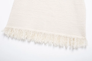Detailaufnahme von cremefarbenem Tweed-Stoff mit Stricktextur und Fransen am Saum