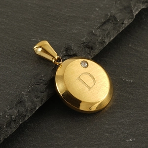 Detailed macro of 18K gold letter D pendant with small diamond on textured slate stone