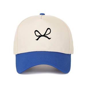 Detail of blue visor and cream five-panel trucker hat with black bow embroidery