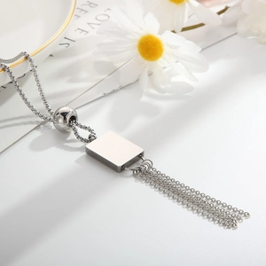 Detail of silver long tassel pendant necklace with square bead on a white ceramic plate