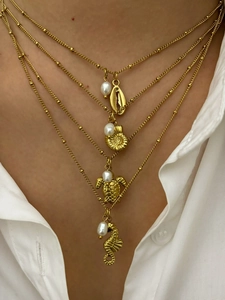 Detail of layered gold necklace featuring seahorse turtle shell pendants and white pearls