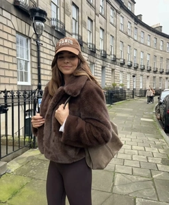 Outdoor street style view of a brown faux fur coat paired with a matching tote and cap