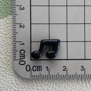 Close-up of mini black resin music note showing 1.2cm size on a measuring ruler