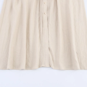 Detailed view of linen texture, pleated front and pearl buttons on a beige shirt dress