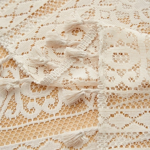 Detail shot of beige lace fabric with intricate crochet patterns and small tassel fringe